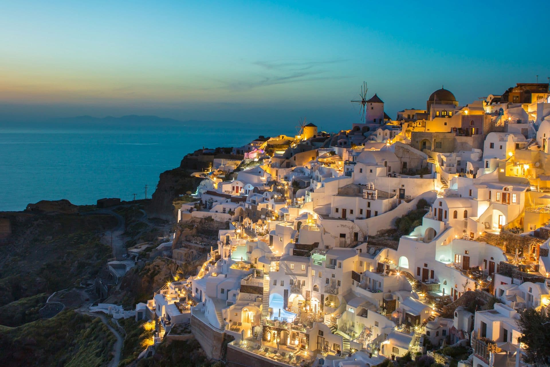 Whitewashed houses and a windmill lit up on the cliffs of Oia, Santorini, at dusk