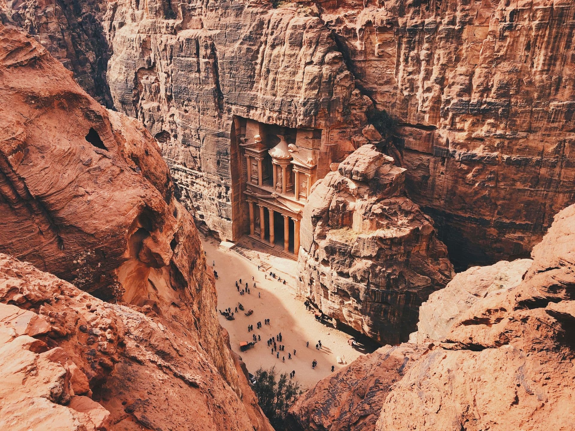 Looking down on the Treasury at Petra from the cliffs above, with visitors in the sandy square below