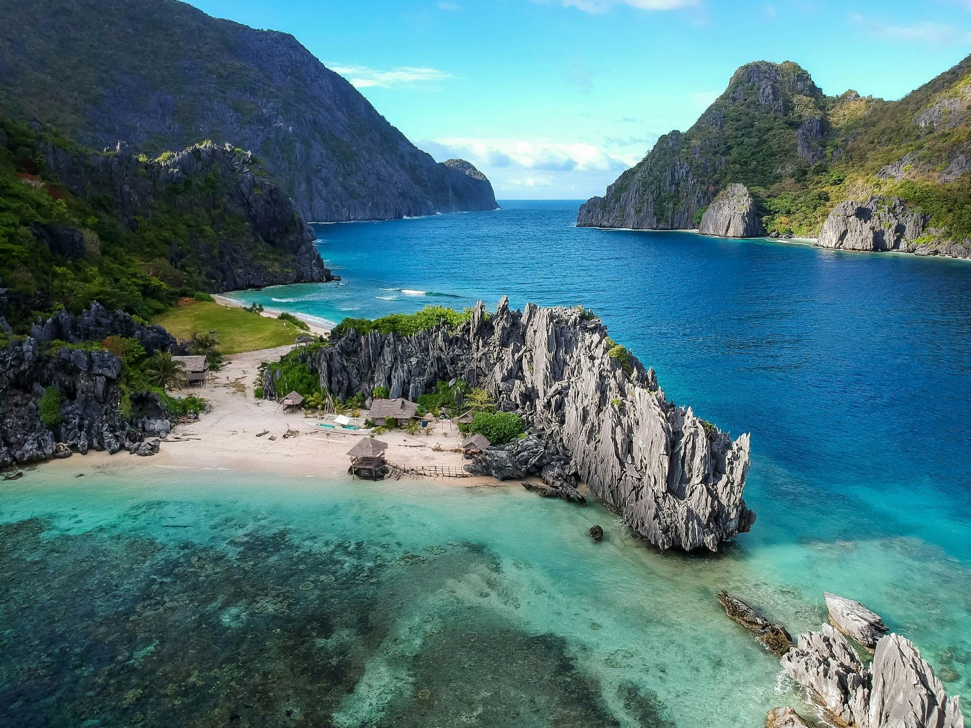 A white sand beach beside jagged limestone rocks and turquoise water, with green islands behind