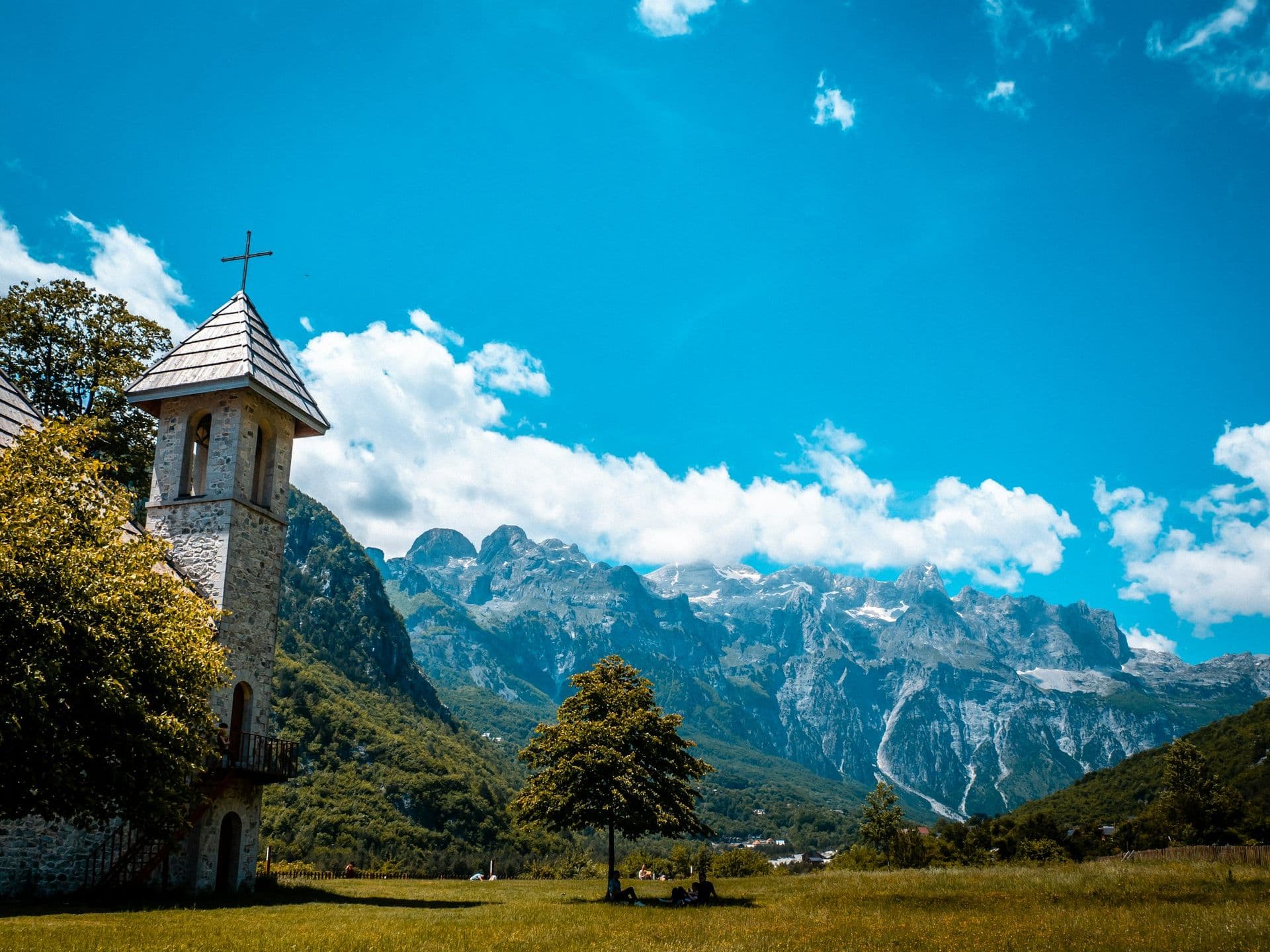 The stone bell tower of Theth church beneath the peaks of the Albanian Alps
