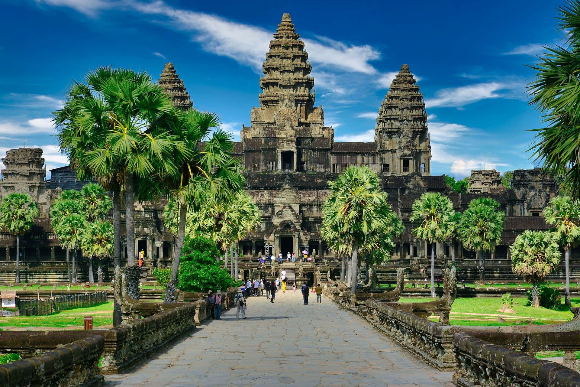 Visitors on the stone causeway leading to the towers of Angkor Wat, lined with palm trees