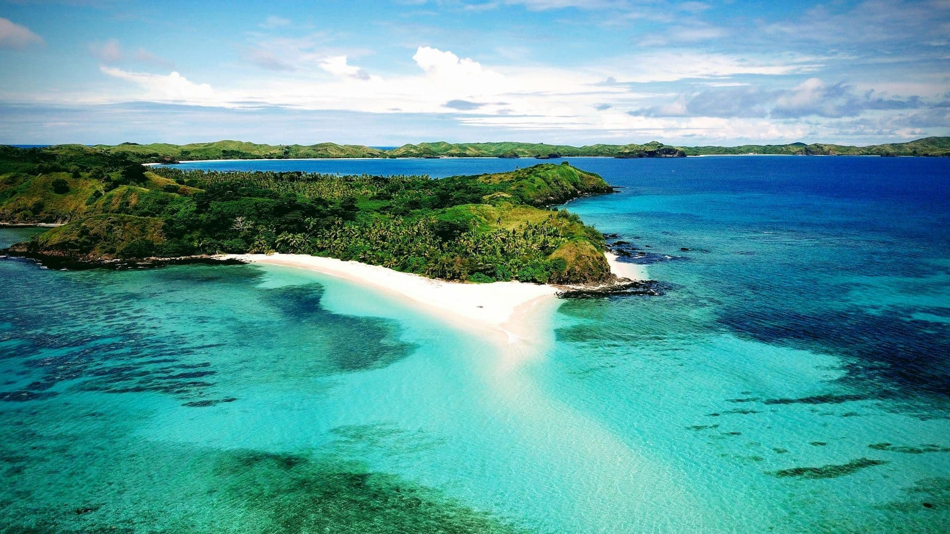A white sand spit reaching into turquoise water off a green Fijian island