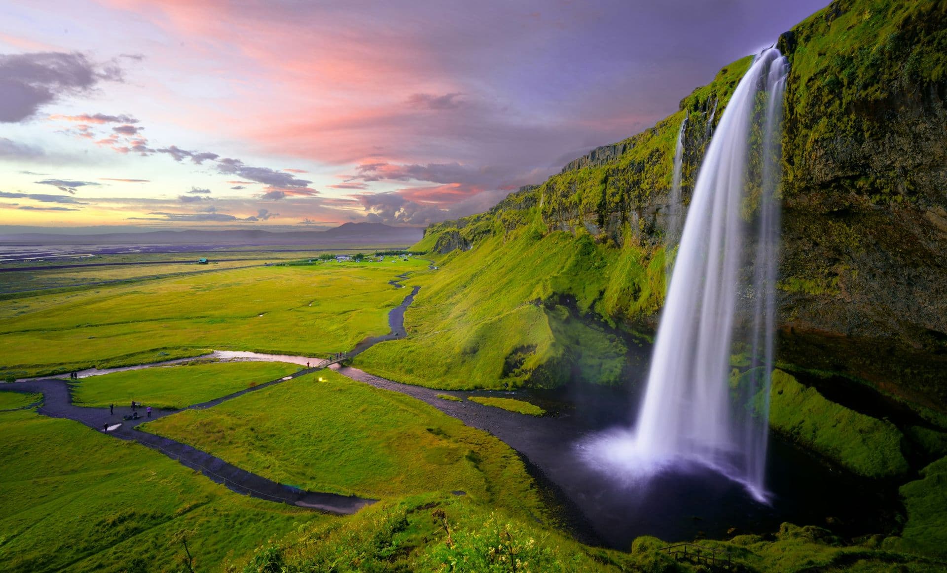Seljalandsfoss waterfall falling into green fields at sunset