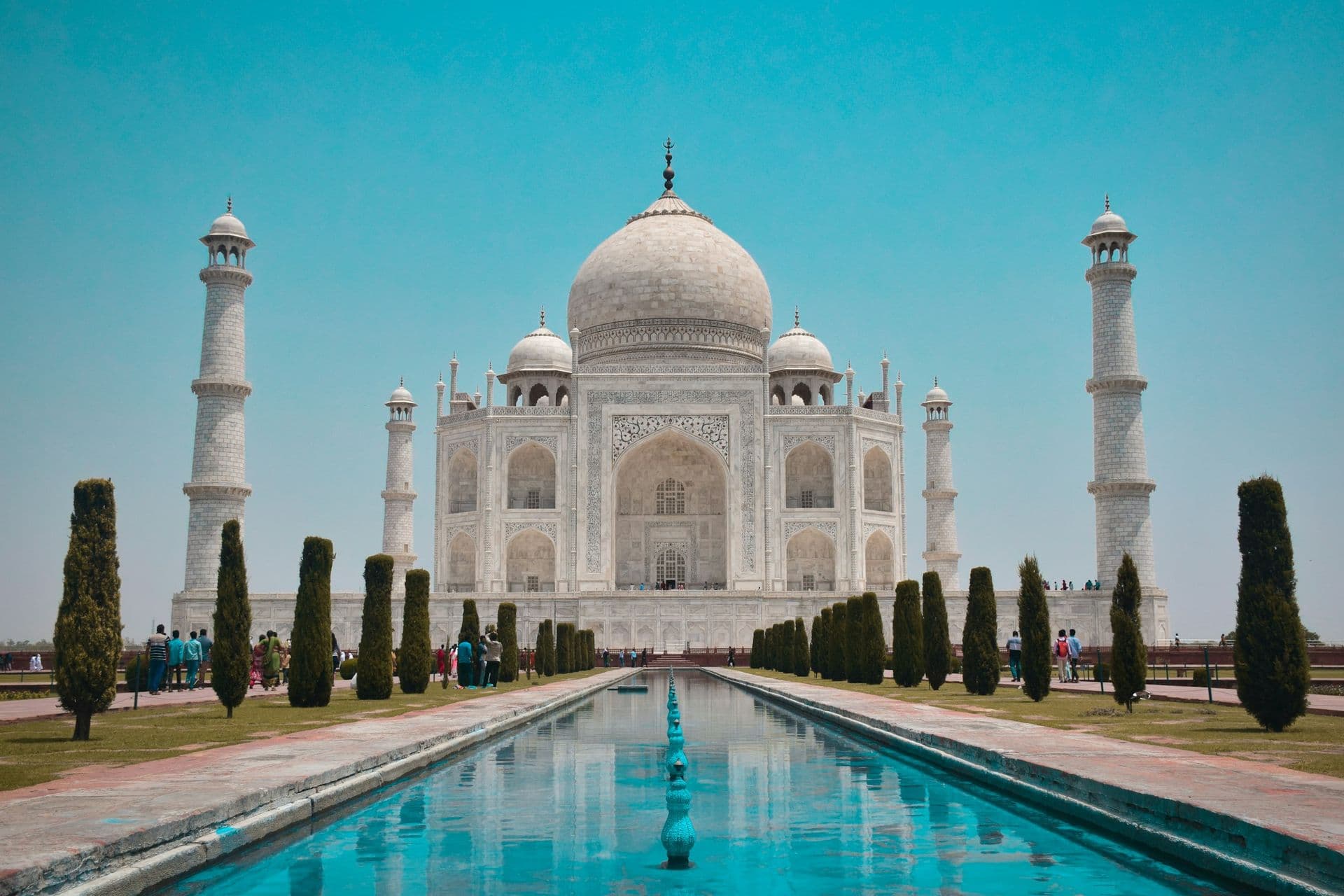 The Taj Mahal and its minarets behind a long reflecting pool lined with cypress trees