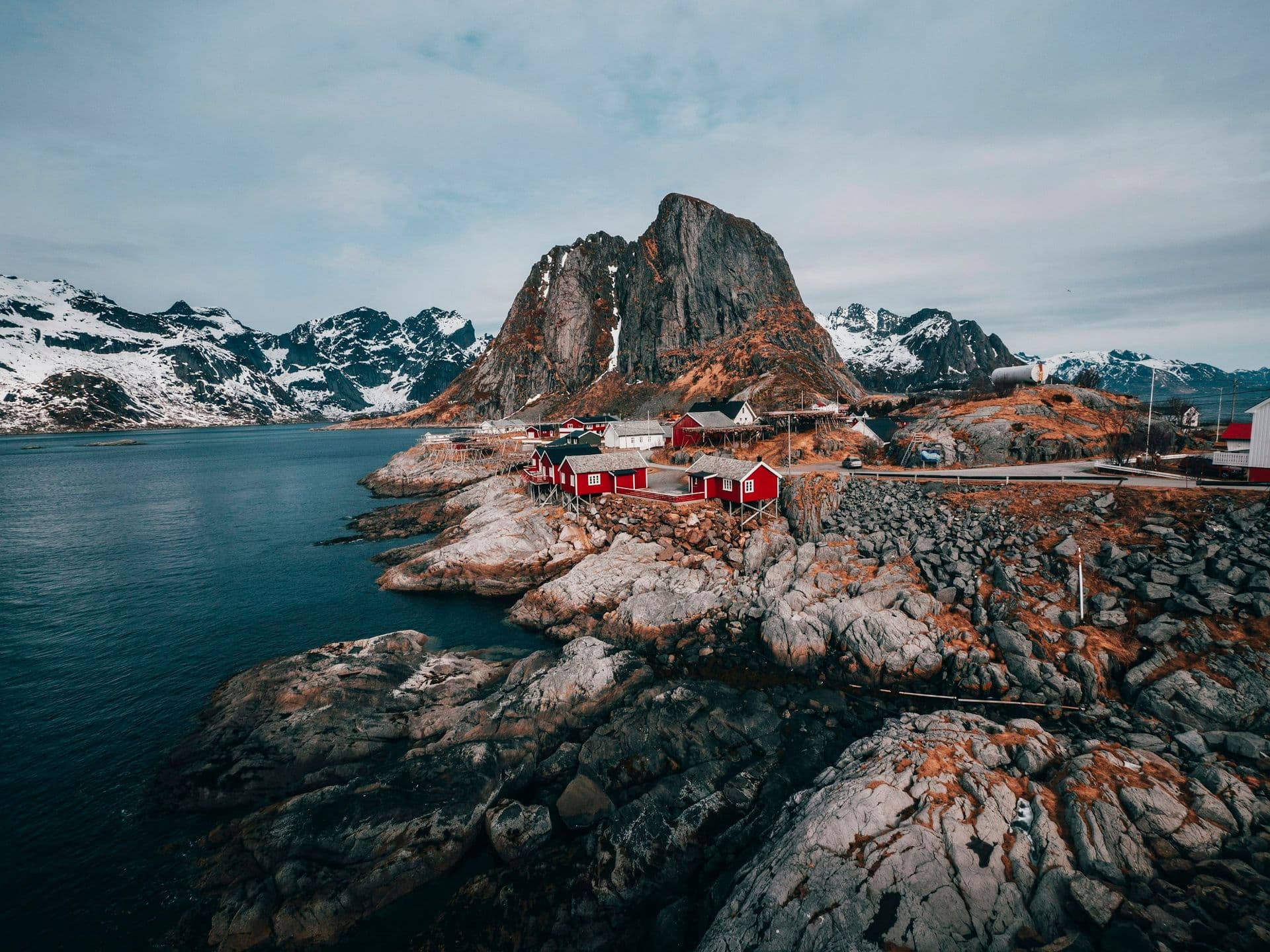 Red fishing cabins on a rocky shore beneath snowy peaks in Lofoten