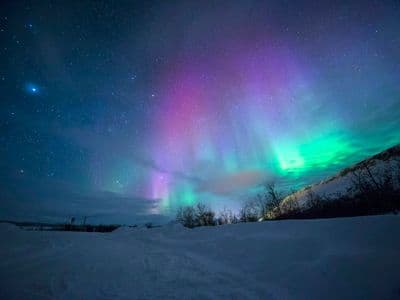 Green and purple northern lights over a snowy landscape