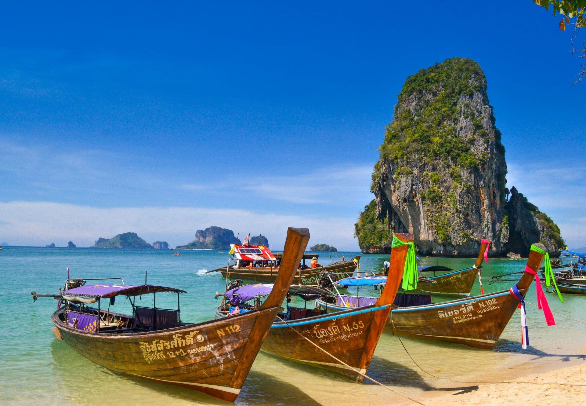 Long-tail boats pulled up on a beach beneath a limestone cliff